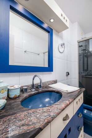 Un baño con un lavamanos azul, azulejos blancos y un espejo grande.