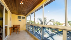 A balcony with a wooden ceiling, a table with chairs, and large windows offering a view of palm trees and buildings. - Apt With Grill 300m From the Beach Mdo201 (Florianópolis)