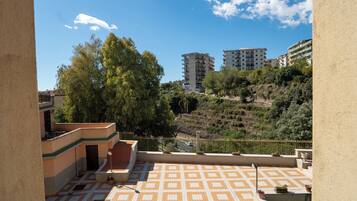 A rooftop terrace with patterned flooring, a railing, and a view of surrounding buildings and trees.