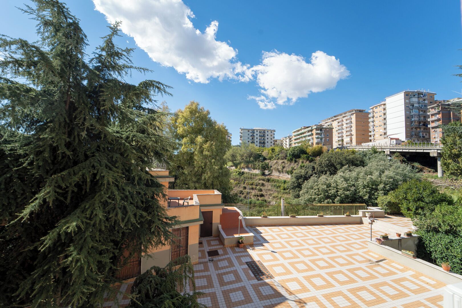 A rooftop terrace with a patterned floor, surrounded by trees and buildings.