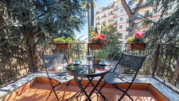 A small outdoor balcony with a round table, two chairs, and potted plants. - Il Cantico Home (Naples)
