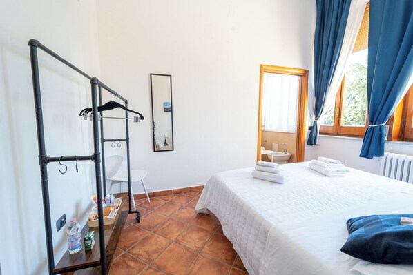 Une chambre d’hôtel avec un lit, une chaise, un miroir, un radiateur et une fenêtre avec des rideaux.
