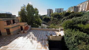 A rooftop terrace with a patterned tile floor, surrounded by greenery and residential buildings.