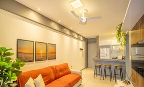 A modern living room with a sofa, a ceiling fan, and a kitchen area with bar stools. - Apart in Condo w/ Pool and Gym Ste0312 (Salvador)