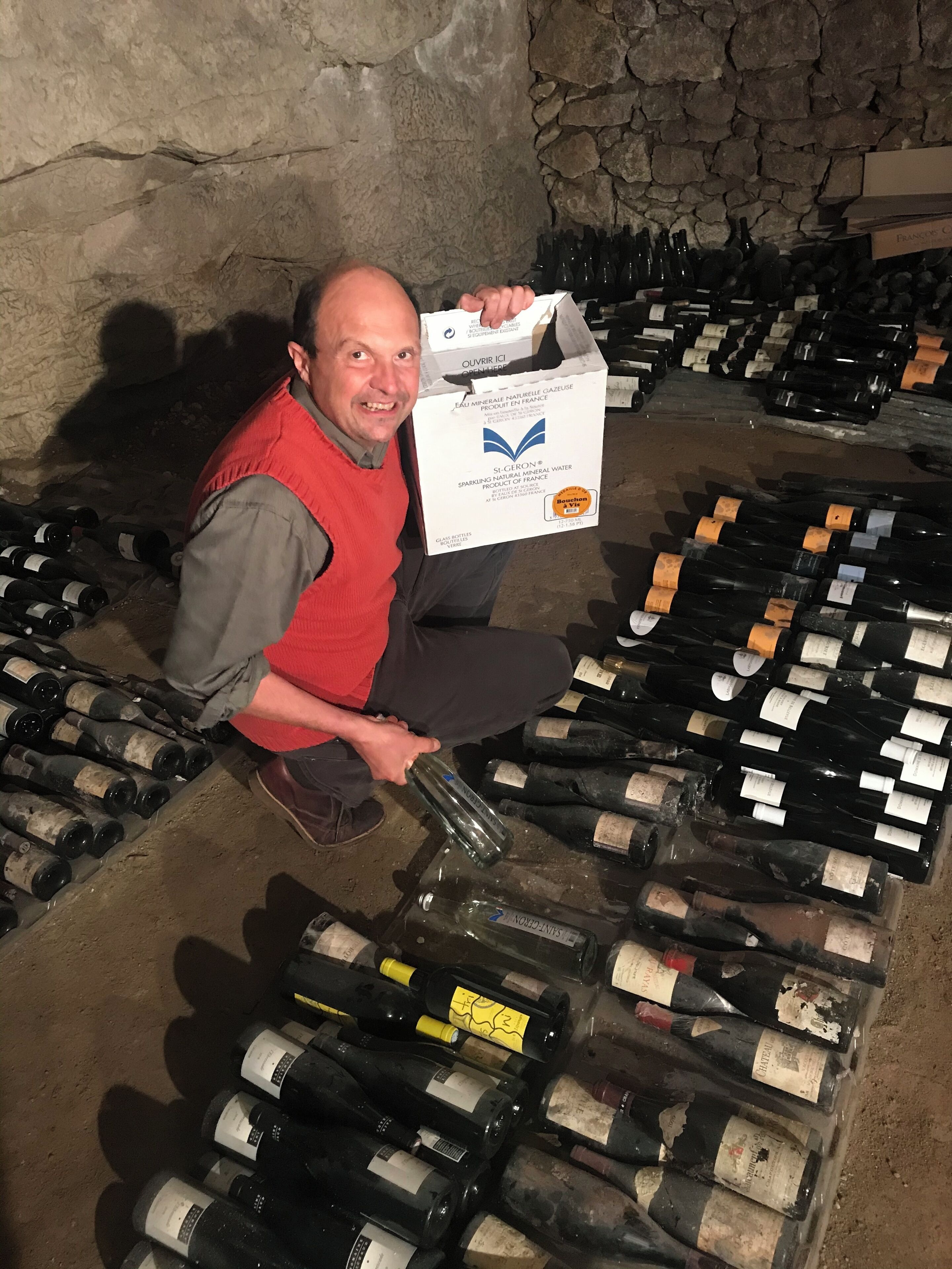 Un hombre sostiene una caja en un sótano lleno de botellas de vino.