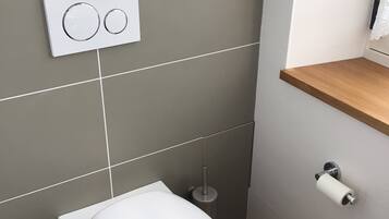 Un baño moderno con inodoro, bidé y cubo de basura.