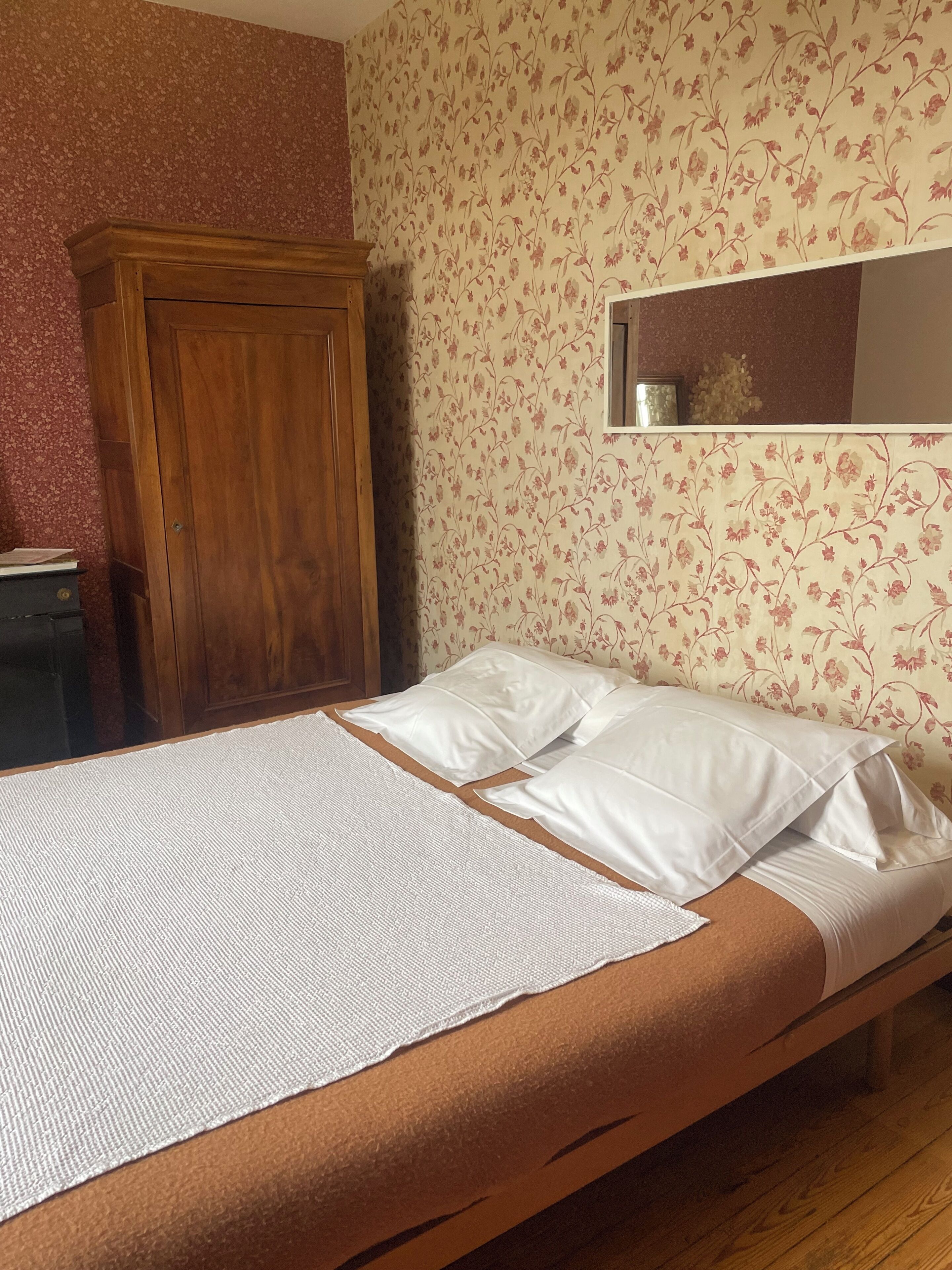 A single bed with white linens, a wooden wardrobe, and floral wallpaper.
