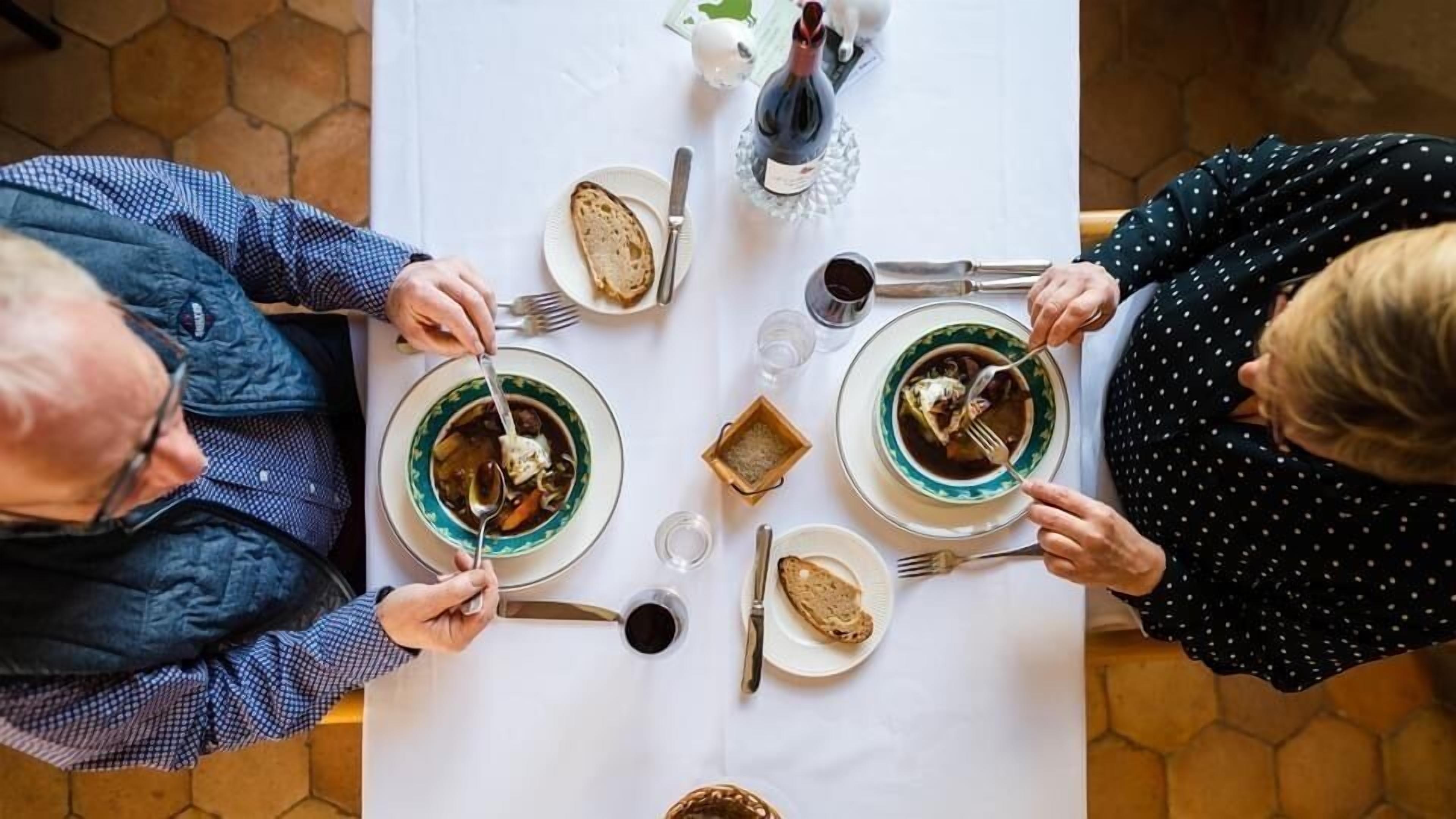 A dining table with plates of soup, bread, and a bottle of wine.