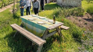 A group of people standing near a stone building with a small tower, a picnic table with plates and a bottle, and a vineyard in the background. - La Galotiere  (Coteaux-sur-Loire)