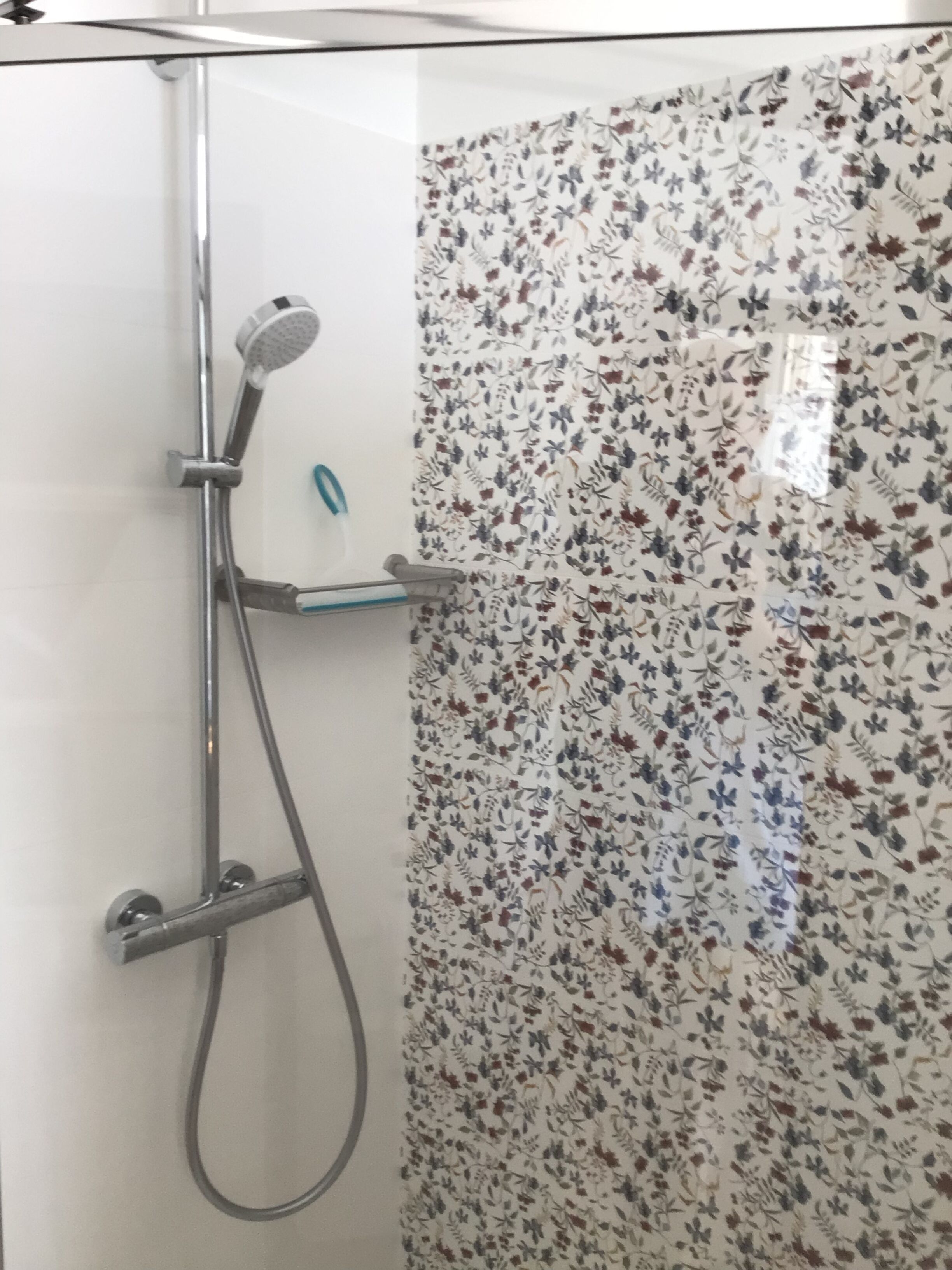 Ducha con patrón de azulejos florales, cabezal de ducha de mano y estante de vidrio.