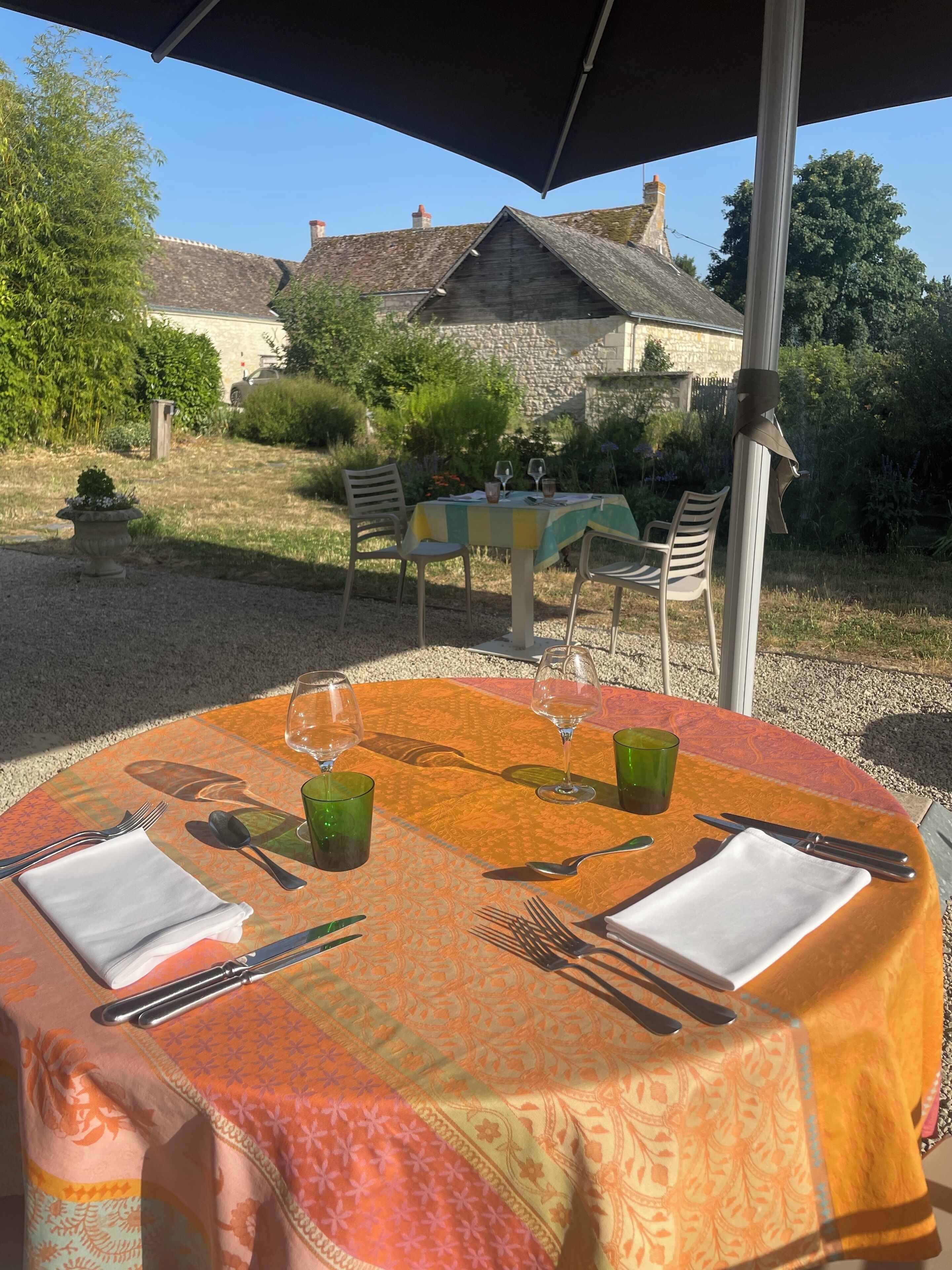 Un espace de restauration en plein air avec une table dressée pour deux personnes, entouré de verdure et bordé d’un mur en pierre.