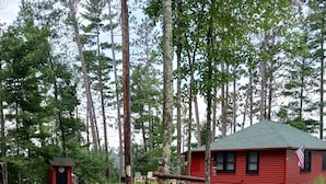 Una cabana rústica amb teulada verda, envoltada d'un jardí ben cuidat i arbres.