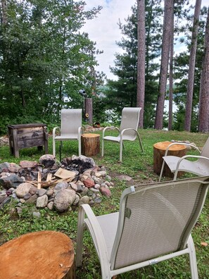 Un espace extérieur aménagé avec des chaises en métal, un foyer entouré de pierres et un banc en bois.