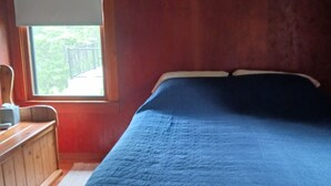 Un dormitori amb un llit gran, un taulell de fusta i una finestra amb vista a vegetació.