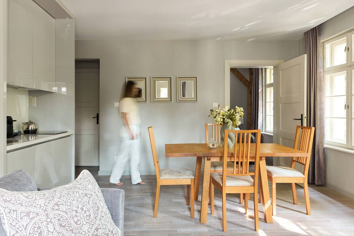 Una sala de estar moderna con una mesa de comedor, sillas de madera y un sofá. Una persona camina por la puerta.
