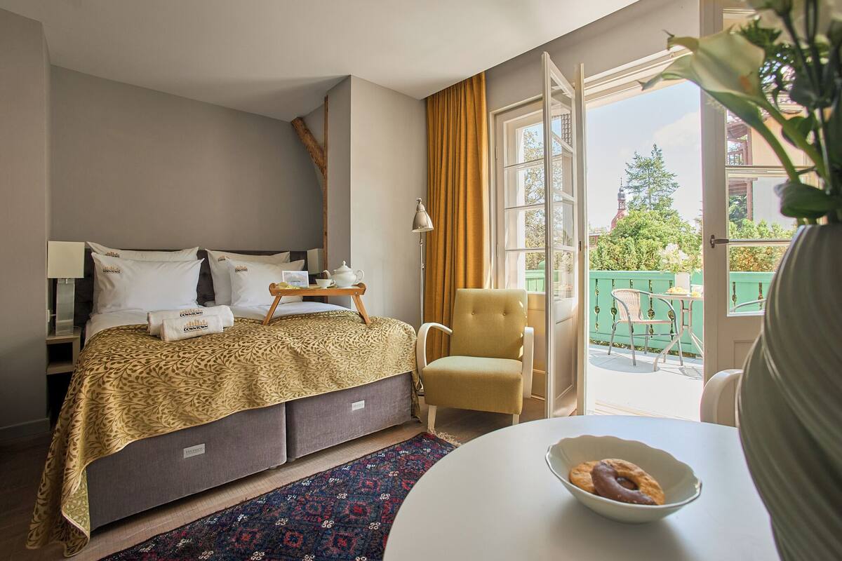 Habitación de hotel con cama, una silla, una mesa con un bol de rosquillas y vistas al exterior.