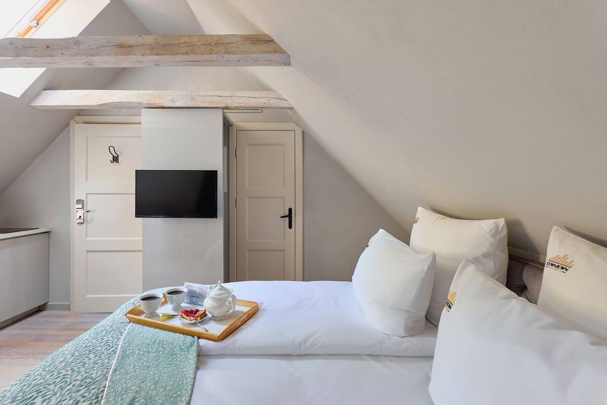 Un dormitorio con cama, almohadas, una bandeja con tazas y una tetera, televisor y una puerta.