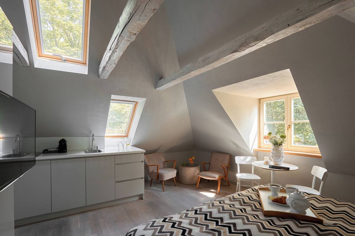 Un dormitorio tipo loft moderno con zona de cocina, ventanas amplias y una acogedora disposición de asientos.