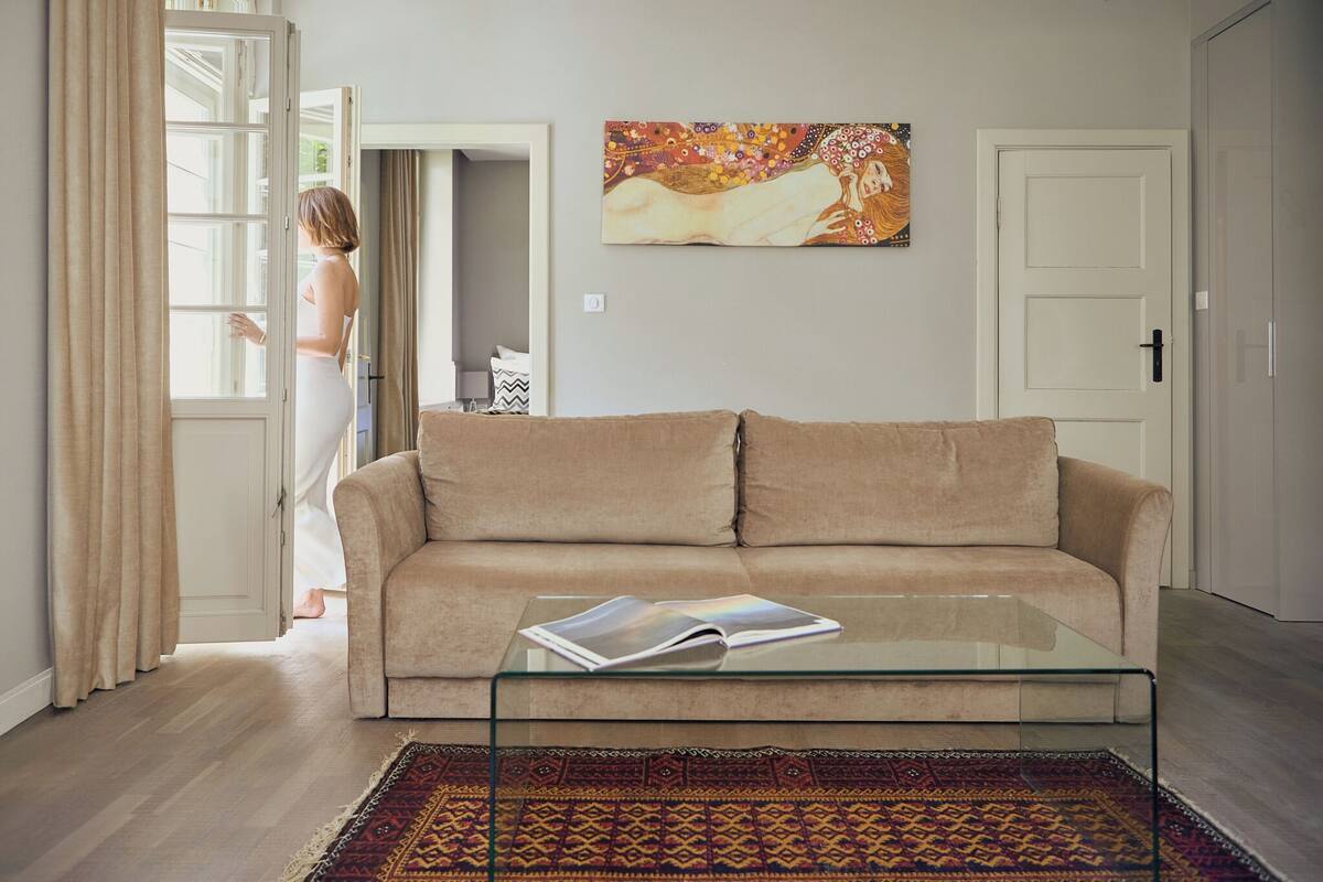 Una sala de estar con un sofá color beige, una mesa de centro de vidrio y una alfombra estampada.