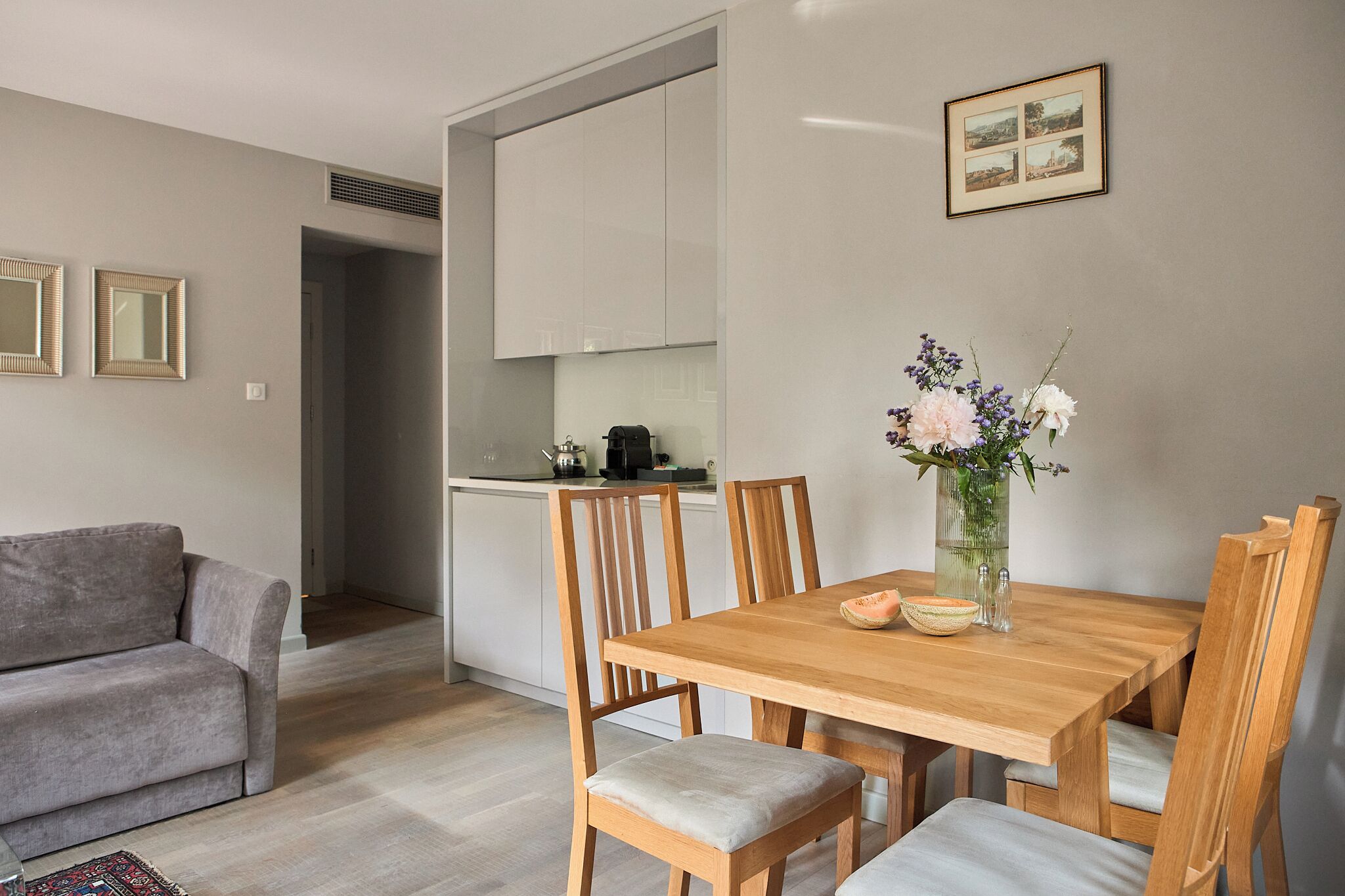 A modern kitchen with white cabinets, a dining table with wooden chairs, and a vase with flowers on the table.