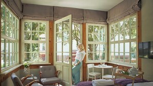 Une pièce avec de grandes fenêtres, un lit, une table avec une théière et deux chaises.