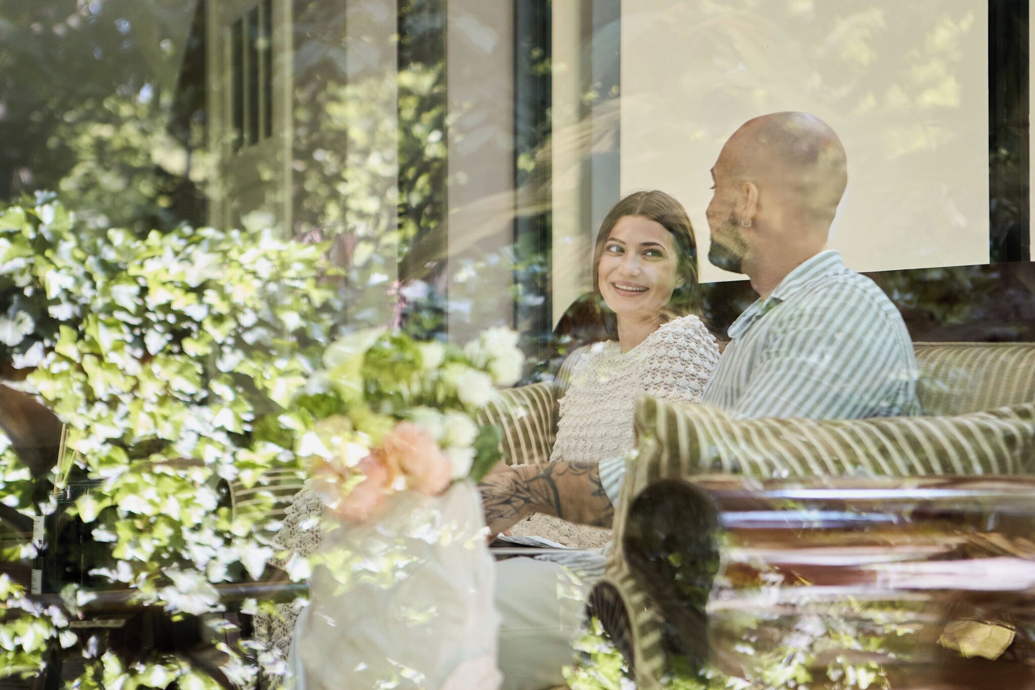 Un couple est assis sur un canapé à rayures, avec vue sur la verdure à l’extérieur.