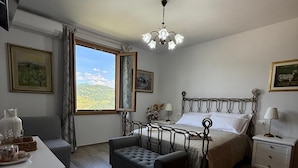 Une chambre à coucher comprenant un lit, des tables de chevet, un banc, un bureau et une fenêtre donnant sur un beau paysage.