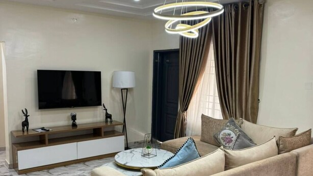 En moderne stue med en beige sofa, et fjernsyn, et konsolbord og et gulv med marmorlook.