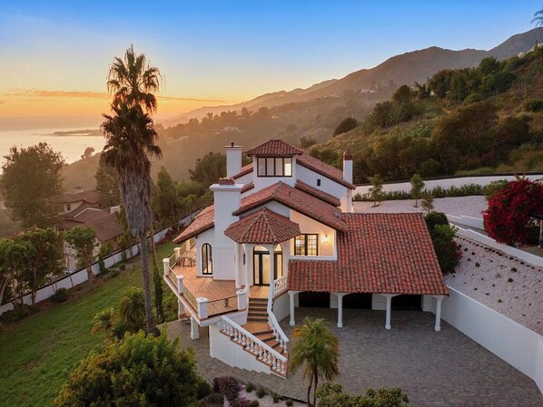 A two-story house with a red-tiled roof, a balcony, and a view of the ocean at sunset. - Villa Costera - Malibu Lookout Mediterranean with Multi-Level Living (Malibu)