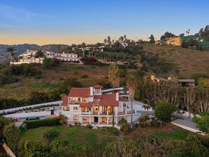 A large, multi-story house with a red-tiled roof, surrounded by lush greenery and hills. - Villa Costera - Malibu Lookout Mediterranean with Multi-Level Living (Malibu)