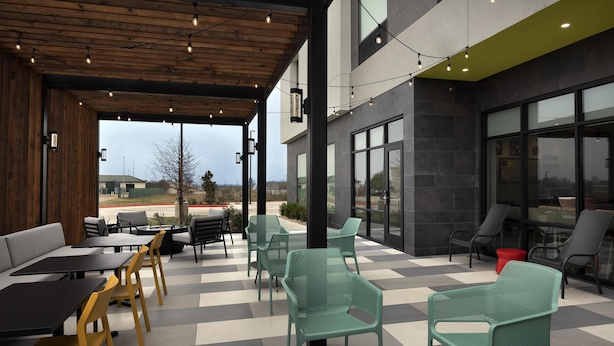 An outdoor seating area with tables and chairs, a wooden ceiling, and large windows. - Home2 Suites By Hilton Taylor (Taylor)