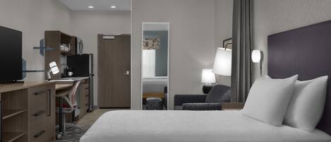 A hotel room with a bed, desk, chair, TV, and a mirror.