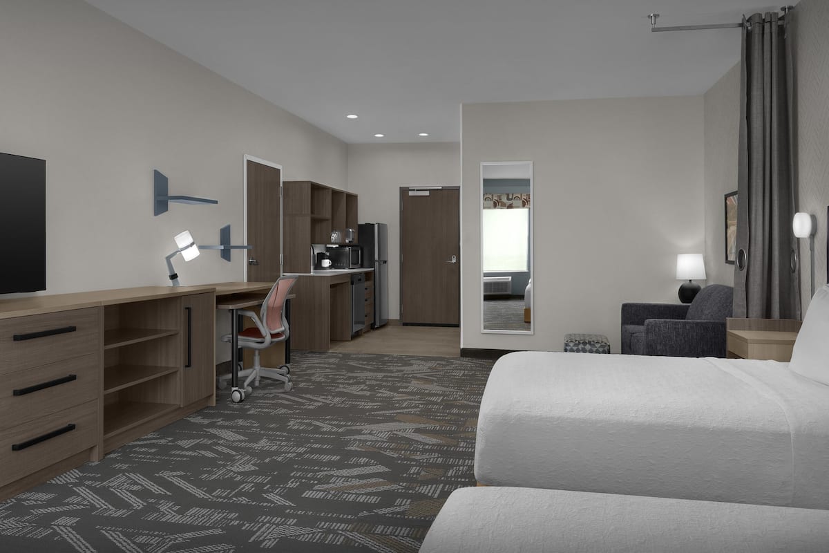 A hotel room with a bed, desk, chair, and a small kitchenette.
