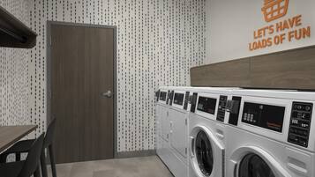 A laundry room with a wall-mounted sign, a wooden door, and a row of washing machines.