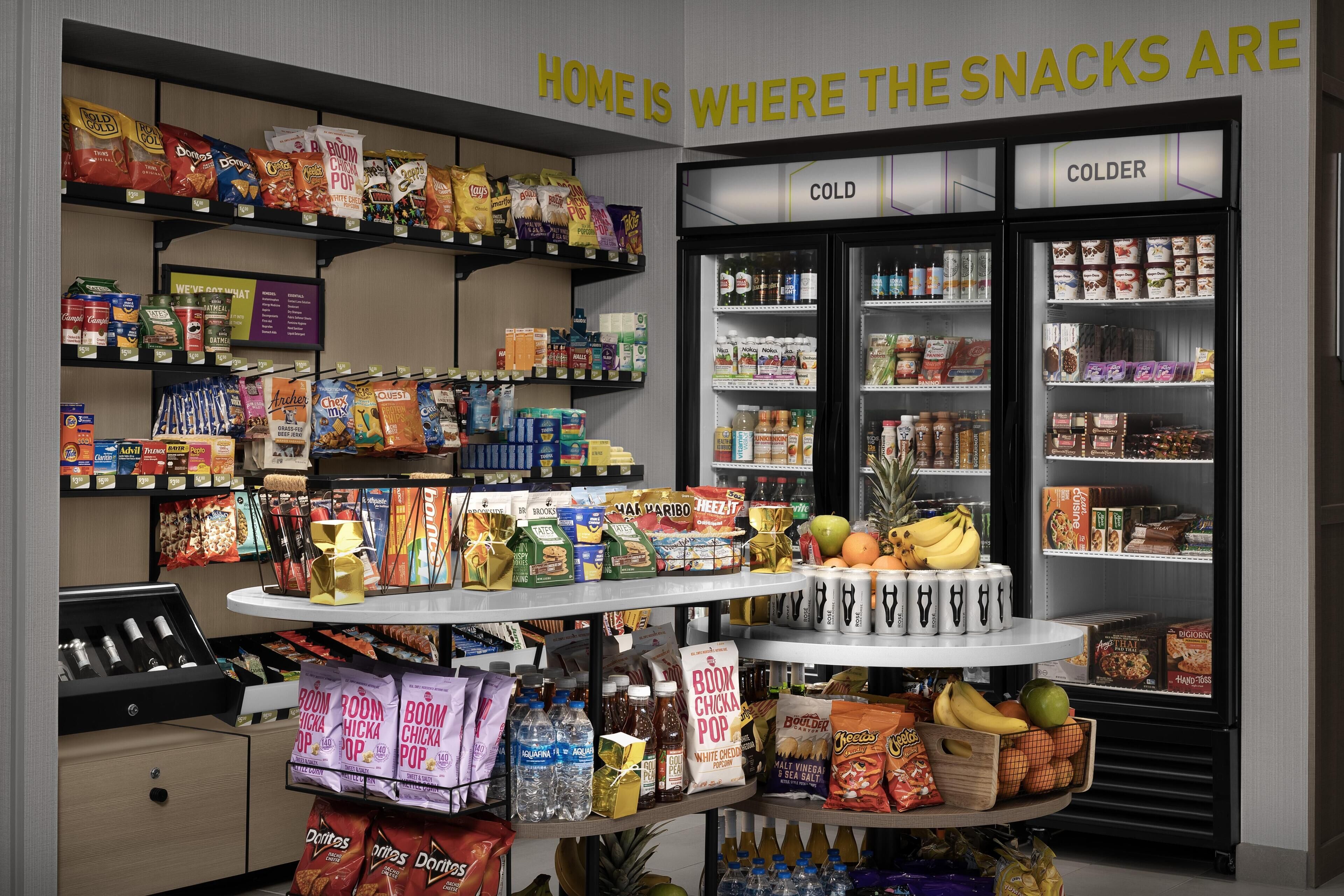 Una tienda de comestibles con estantes llenos de refrigerios, una sección con neveras y una exhibición de agua embotellada y bocadillos.
