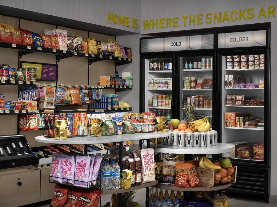 Una tienda de comestibles con estantes llenos de refrigerios, una sección con neveras y una exhibición de agua embotellada y bocadillos.