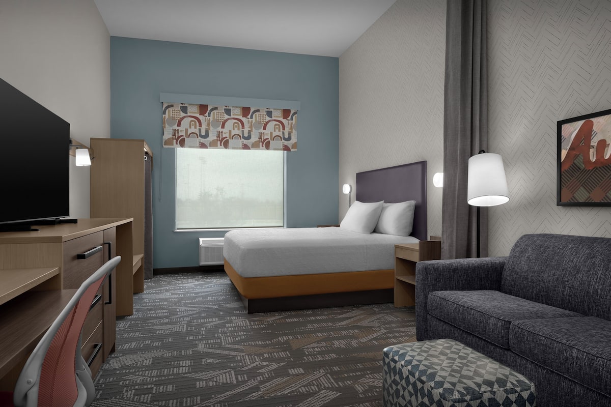 A hotel room with a bed, desk, chair, and a couch.