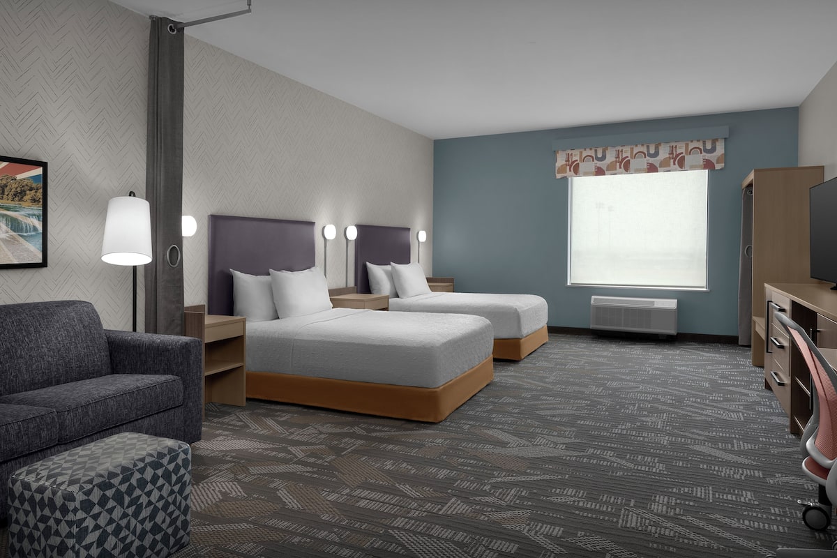 A hotel room with two beds, a sofa, a desk, and a TV.