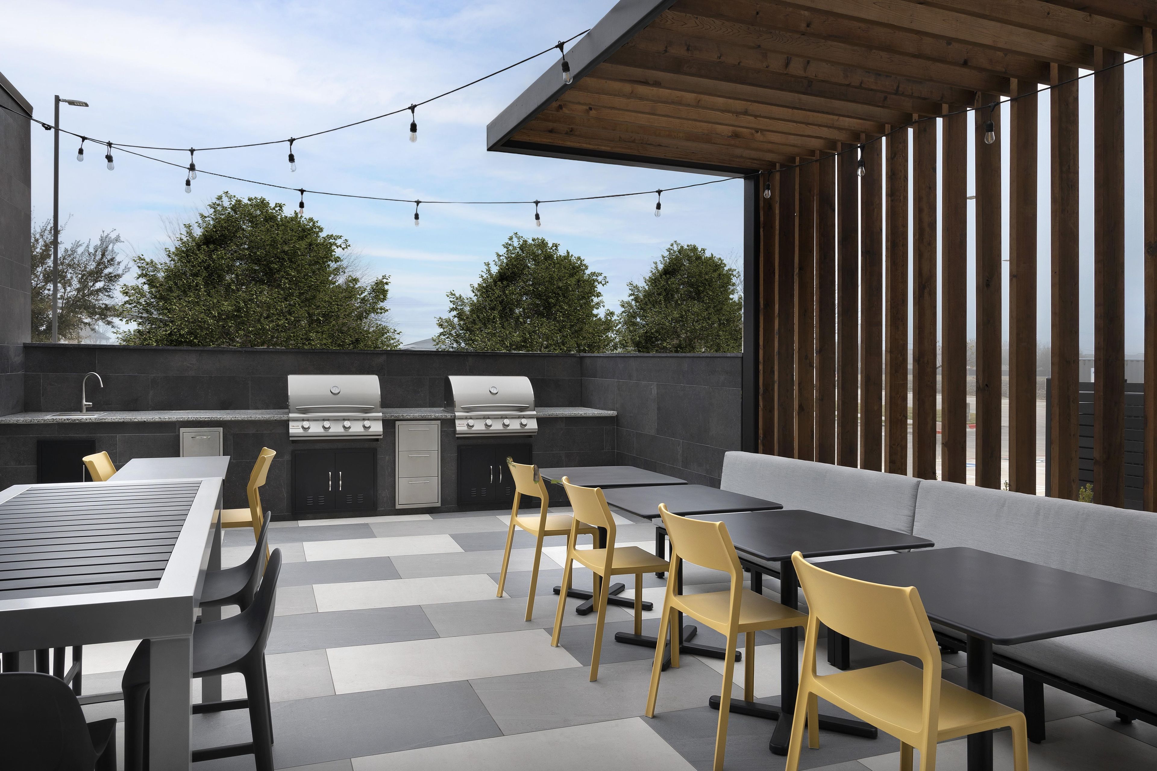 An outdoor patio with a barbecue grill, seating area, and string lights.