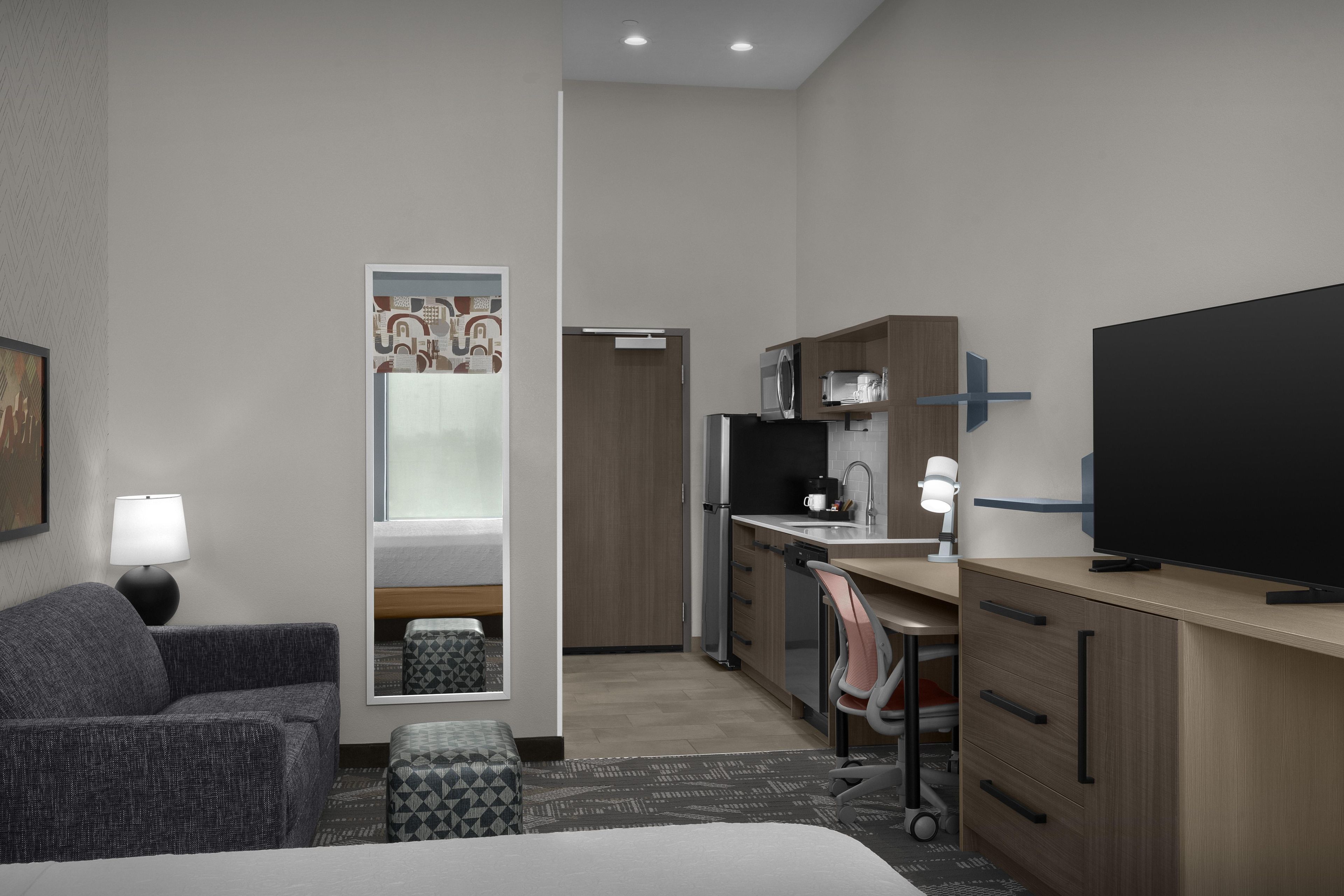 A hotel room with a bed, a desk, a television, and a kitchenette.