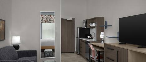 A hotel room with a bed, a desk, a television, and a kitchenette.