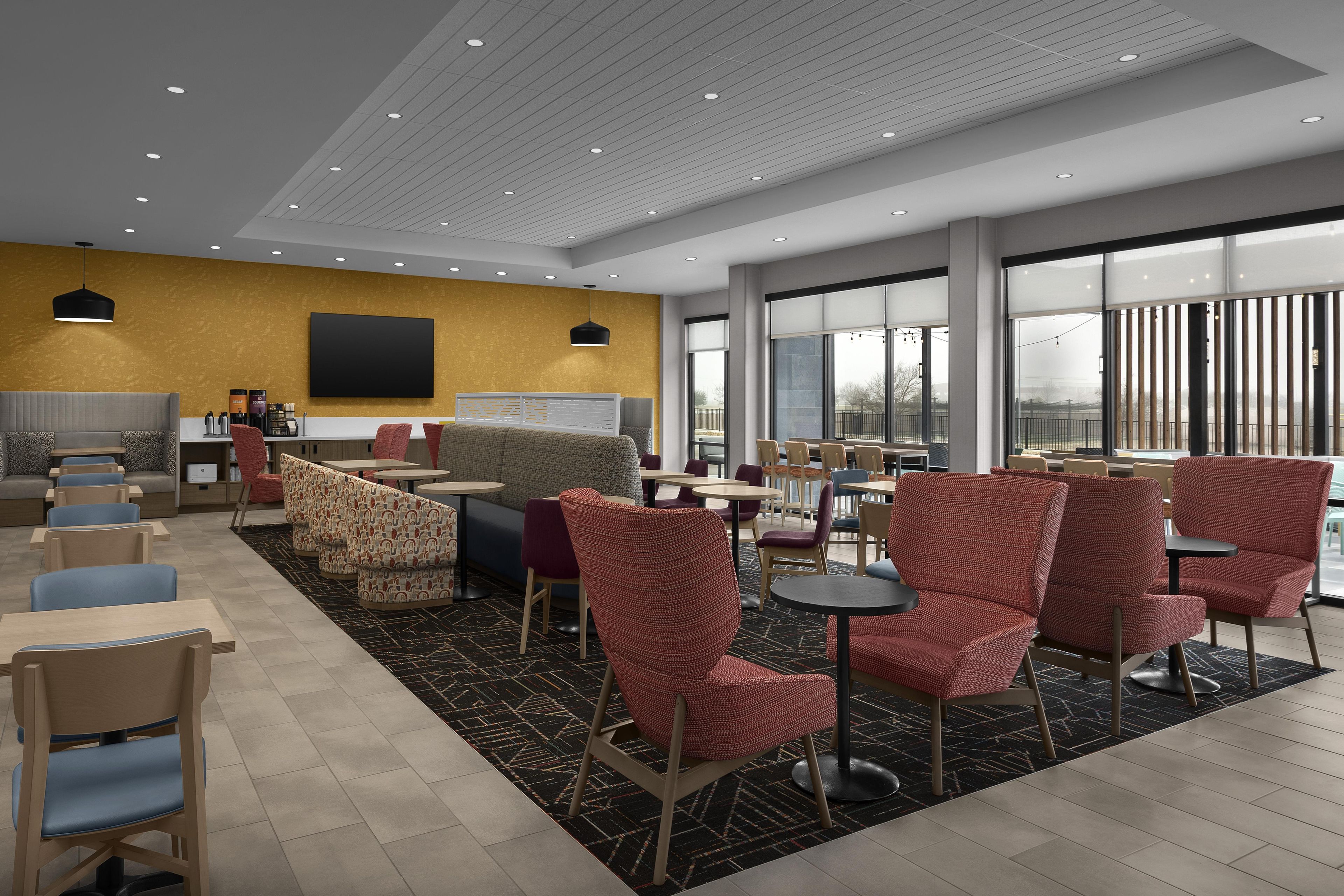 A modern indoor seating area with multiple tables and chairs, a large window offering a view, and a flat-screen TV mounted on the wall.