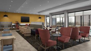 A modern indoor seating area with multiple tables and chairs, a large window offering a view, and a flat-screen TV mounted on the wall.