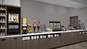 A self-service breakfast station with yogurt dispensers, fruit, and coffee machines. - Home2 Suites By Hilton Taylor (Taylor)