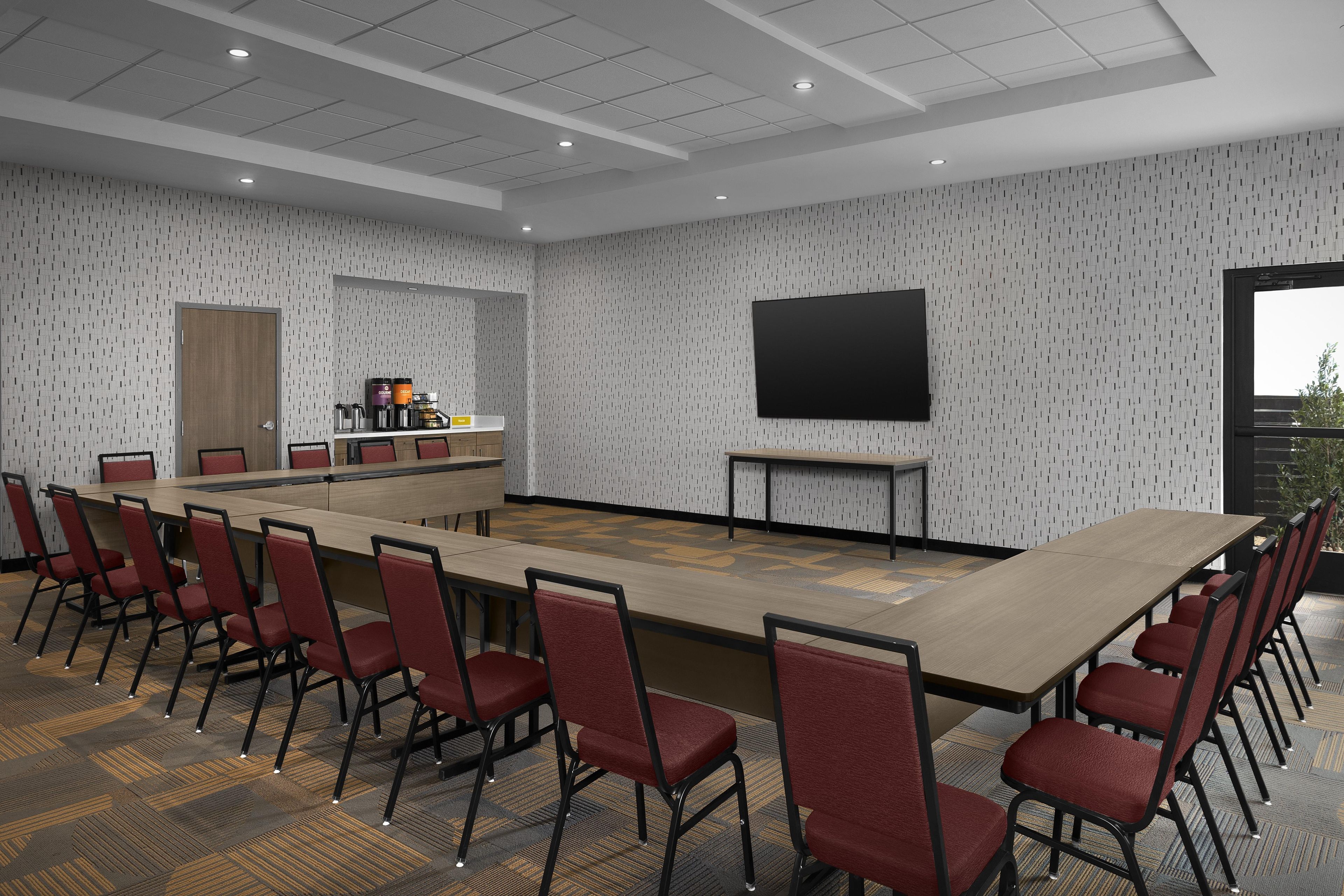 A conference room with a long table, red chairs, a coffee station, a large screen, and patterned walls.