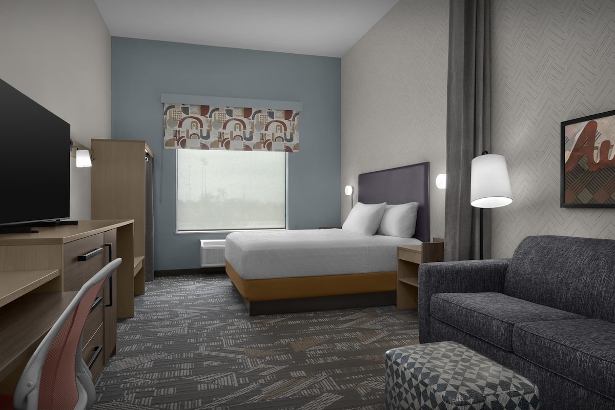 A hotel room with a bed, a desk, a chair, a sofa, and a TV.