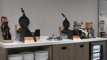 Angolo cottura con piastre per waffle, macchine da caffè e frigorifero fornito di bevande.