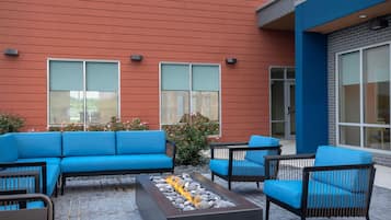 An outdoor seating area with a blue sofa, chairs, and a fire feature.