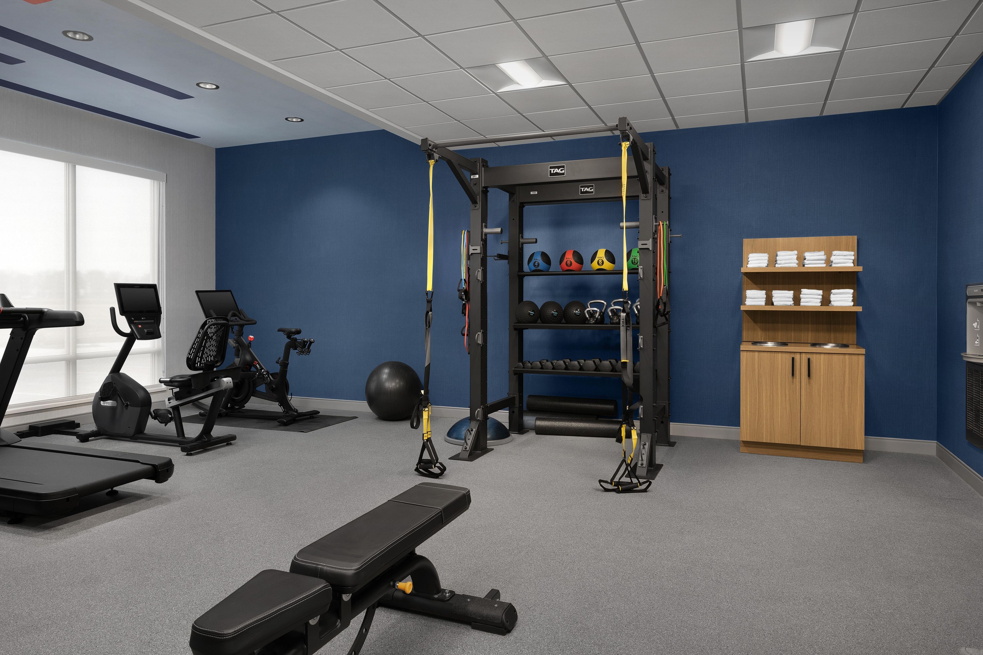 A gym with exercise equipment, a bench, a squat rack, and a wall-mounted shelf with towels.