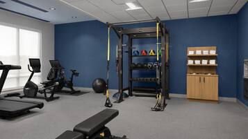 Un gimnasio con equipo de ejercicio, una banca, una jaula para sentadillas y un estante en la pared con toallas.